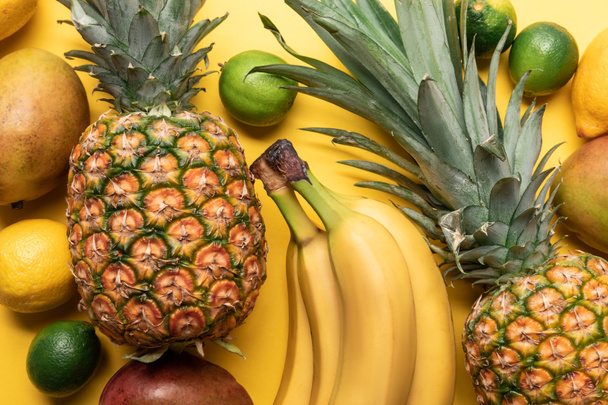 vista superior de plátanos maduros enteros, piña, cítricos y mango sobre fondo amarillo
 - Foto, Imagen
