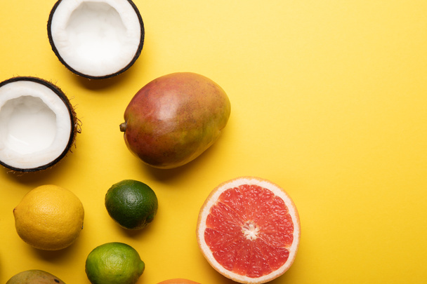 top view of citrus fruits, mango and coconuts on yellow background with copy space - Fotó, kép