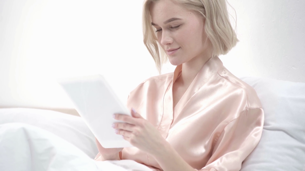 felice ragazza bionda utilizzando tablet digitale e sorridente a letto
  - Filmati, video