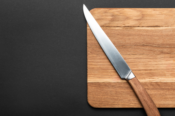 top view of knife and wooden cutting board on black background - Photo, Image
