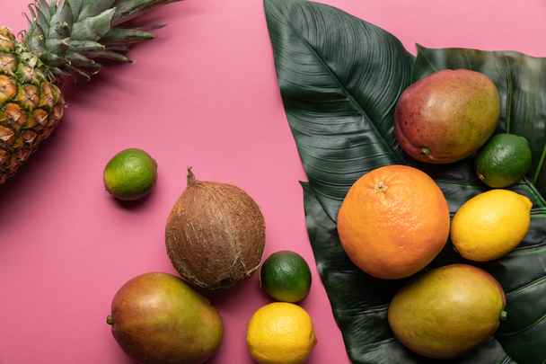 top view of ripe tropical bright fruits with green leaves on pink background  - Fotoğraf, Görsel