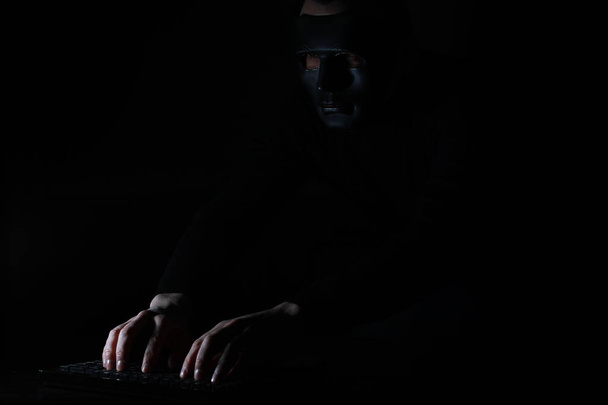 Un hombre con una máscara imprime en el teclado en la oscuridad
 - Foto, Imagen