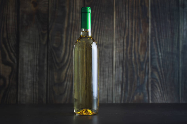Průhledná láhev bílého suchého vína na stole. Bílé vinné sklo na dřevěné stěně pozadí. - Fotografie, Obrázek