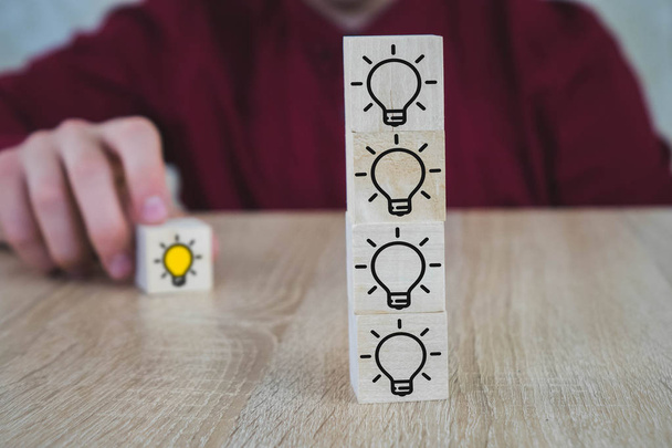 Handverlesen steht ein Holzwürfel mit dem gelben Glühbirnensymbol auf dem Holztisch. Neue Idee, Innovation und Lösungskonzepte. - Foto, Bild