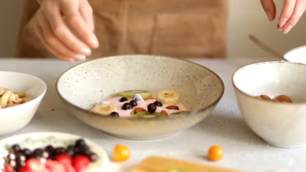 A woman prepares a delicious and healthy Breakfast in the morning in the kitchen, hands puts on yogurt berries, fruits and nuts, closeup - Filmagem, Vídeo