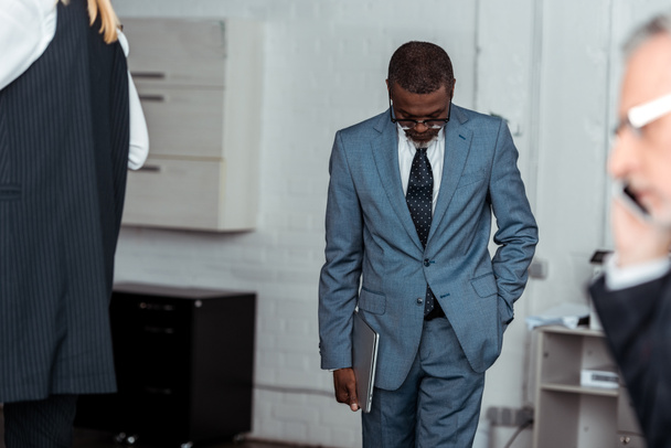 enfoque selectivo de hombre de negocios afroamericano sosteniendo portátil cerca de los socios
 - Foto, Imagen