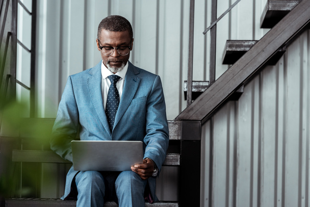 handsome african american man in glasses using laptop in office  - Fotografie, Obrázek