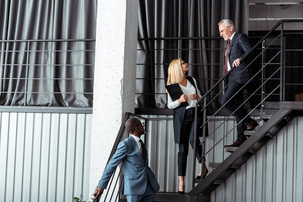 femme d'affaires heureuse regardant homme d'affaires près de l'homme afro-américain marchant dans les escaliers
  - Photo, image