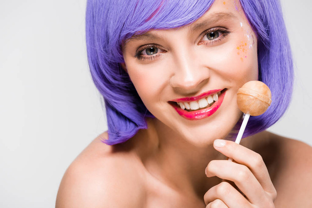 красива усміхнена дівчина в фіолетовій перуці тримає солодкі цукерки, ізольована на сірому
 - Фото, зображення