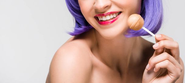 cropped view of smiling nude girl in purple wig holding sweet lollipop, isolated on grey - Фото, изображение