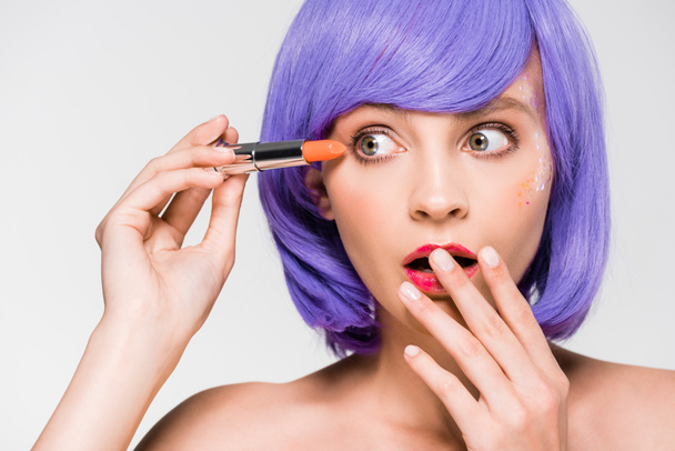 stylish shocked girl in purple wig holding lipstick isolated on grey - Foto, Imagen