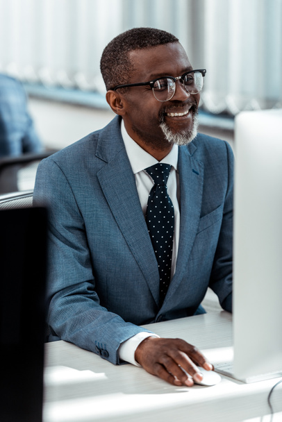 selective focus of happy african american businessman looking at computer monitor in office  - Fotoğraf, Görsel