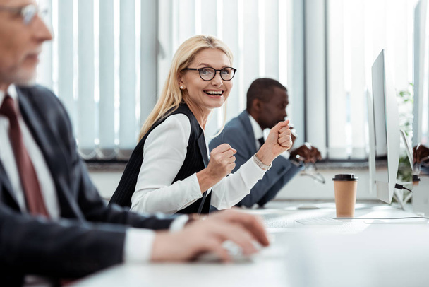 selective focus of cheerful businesswoman smiling near men in office  - Photo, Image