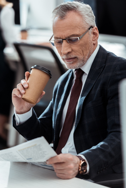 guapo hombre de negocios mirando el periódico mientras sostiene la taza desechable
  - Foto, imagen