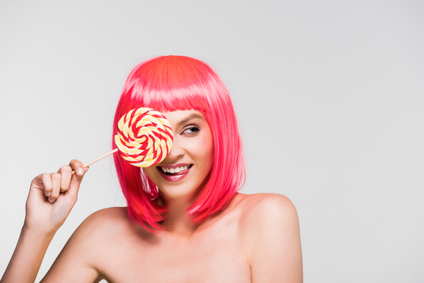 smiling pretty girl in pink wig holding sweet lollipop, isolated on grey - Foto, Bild