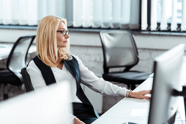 επιλεκτική εστίαση της ξανθιά επιχειρηματίας σε γυαλιά που κάθονται στο γραφείο  - Φωτογραφία, εικόνα