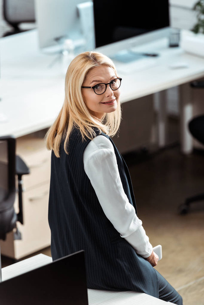 overhead view of attractive blonde businesswoman in glasses smiling in office  - Fotó, kép