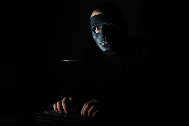 Maskeli bir adam karanlıkta klavyeye baskı yapmış. - Fotoğraf, Görsel