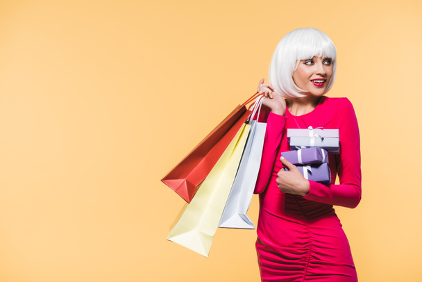 attractive woman with gifts and shopping bags, isolated on yellow - Photo, Image