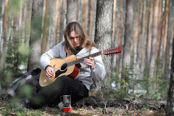 Κιθαρίστας στο δάσος σε ένα πικνίκ. Ένας μουσικός με ένα ακουστικό  - Φωτογραφία, εικόνα