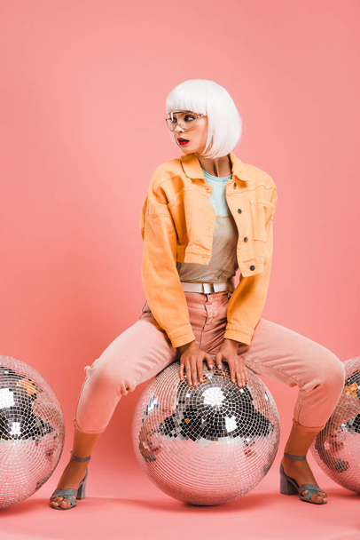 stylish model in white wig posing with disco balls on pink - Zdjęcie, obraz