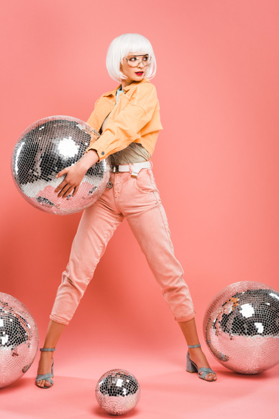 fashionable woman in white wig posing with disco balls on pink - Fotó, kép