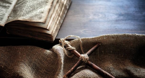Livro velho religioso em uma mesa de madeira. Uma cruz religiosa amarrada com uma corda e uma serapilheira ao lado da Bíblia. Adoração, pecados e oração
 - Foto, Imagem