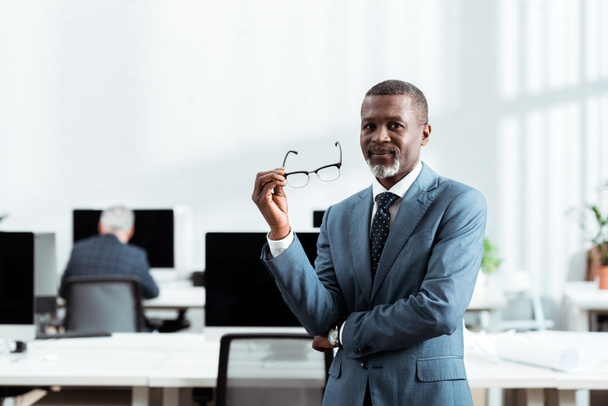 オフィスで眼鏡を持つアフリカ系アメリカ人ビジネスマンの選択的焦点  - 写真・画像