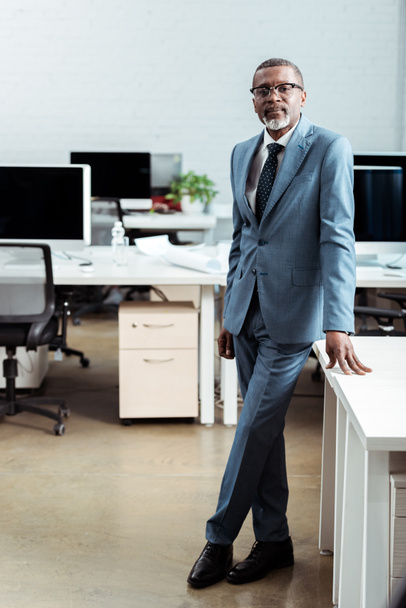 handsome african american man in glasses standing in suit in modern office  - Фото, зображення