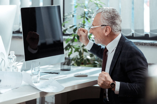 homem de negócios feliz em óculos gesticulando perto do monitor do computador com tela em branco
  - Foto, Imagem
