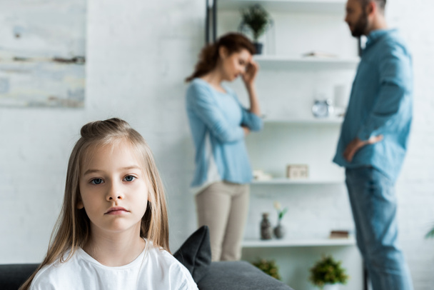 selective focus of upset kid looking at camera near quarreling parents at home - Photo, Image