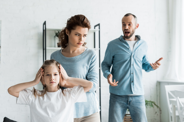 selective focus of mother covering ears on daughter while man screaming at home  - Foto, Imagem