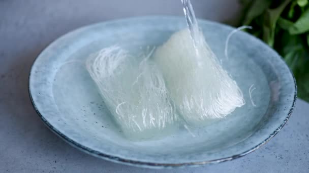 Rice glass noodles preparation. Pouring hot water in bowl with dry asian rice vermicelli or noodles - Πλάνα, βίντεο