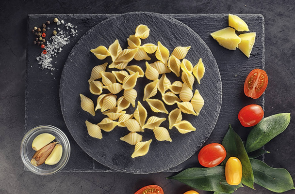 Pasta shells on black stone. Tomatoes and bay leaves with allspice and sea salt and garlic. - Photo, Image