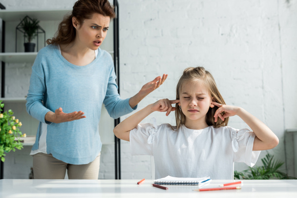 boos moeder gebaren terwijl praten in de buurt van dochter met gesloten ogen  - Foto, afbeelding