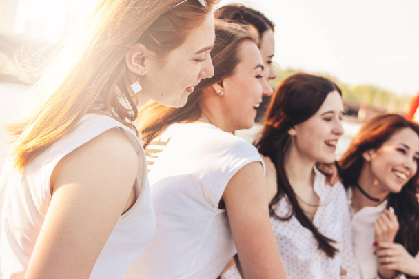 Groep van jonge gelukkige meisjes vrienden genieten van het leven op de zomerstad straat, zonsondergang achtergrond - Foto, afbeelding