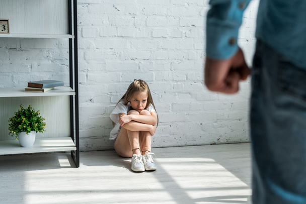 selective focus of scared kid sitting on floor and looking at father at home  - Foto, afbeelding