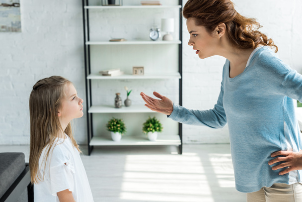 frustrated mother standing with hand on hip and gesturing near daughter  - Foto, Bild