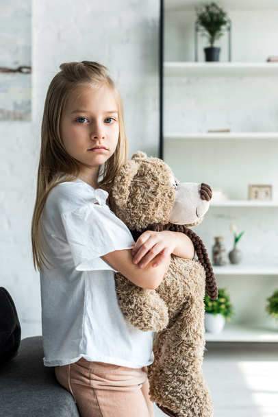 cute kid looking at camera and holding teddy bear at home  - Foto, immagini
