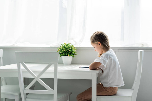 cute kid sitting and writing in notebook at home  - Foto, Imagen