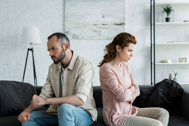 upset woman sitting near angry husband with crossed arms at home  - Foto, Imagen