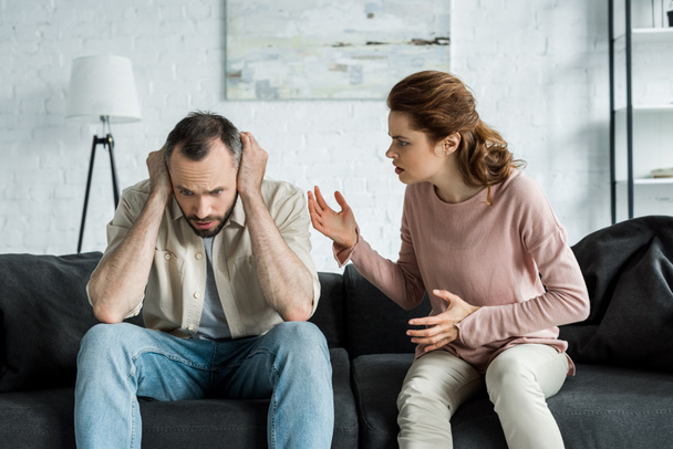 upset woman gesturing and looking at man covering ears at home  - Photo, Image