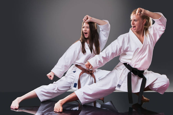 Two beautiful young female karate players doing kata on the gray background - Foto, immagini