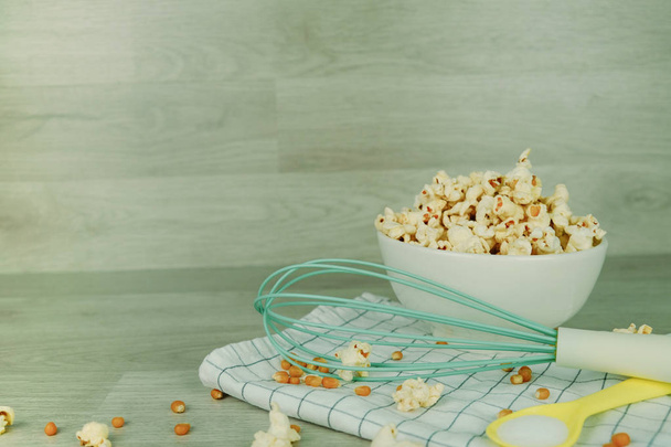 Popcorn in witte kom met pastel lepel, zout, hand mixer - Foto, afbeelding