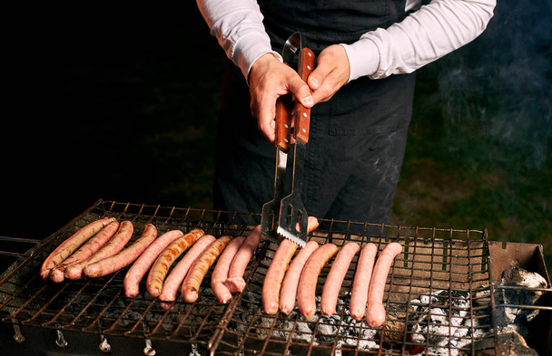 Cropped image of man cooking sausages on grill  - Фото, зображення