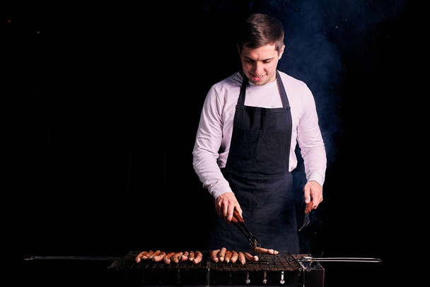Young man grilling sausages outdoors - Фото, изображение