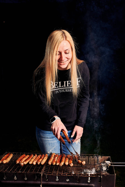 Beautiful young woman grilling sausages  - Фото, зображення