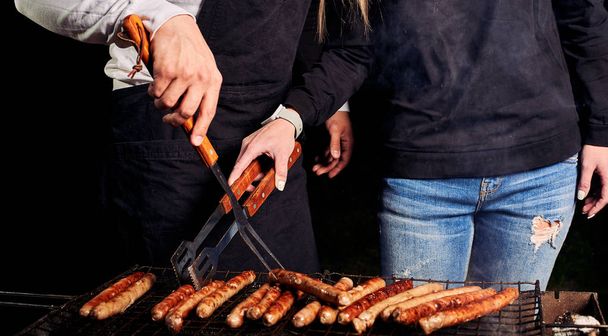 Partial shot of couple grilling sausages outdoors  - Fotoğraf, Görsel