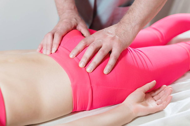 Close-up of a young girls spine base editing by a male physiotherapist of visceral massage. The hands of the doctor set and knead the tailbone of the patient - Photo, Image