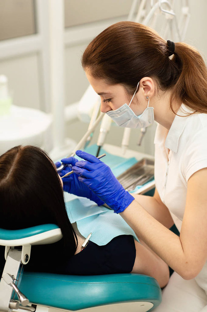 Closeup portrait of young woman patient, sitting in dentist chair. Doctor examines the teeth. Dental health prevention - Photo, image